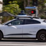 A Waymo autonomous vehicle operating on a tree-lined street in Santa Monica.