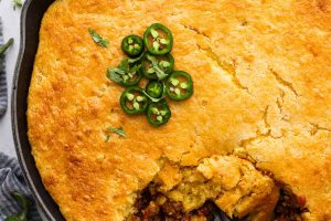 Overhead shot of cowboy cornbread casserole with a garnish jalapeños on top and a spoon scooping some out.