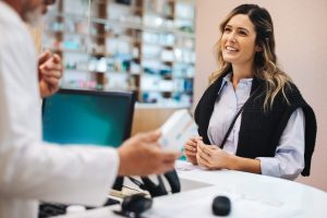 Smiling woman at the pharmacy getting prescription filled and receiving medicine from the pharmacist