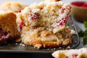 Side shot of raspberry muffin cut in half sitting on top of a pan of raspberry muffins.