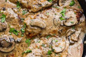 Overhead shot of skillet filled with smothered chicken with wooden spoon sticking out.