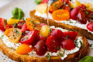 Side shot of someone drizzling olive oil over tomato toast.