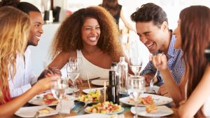 A group of friends smile and laugh while enjoying a meal at a restaurant