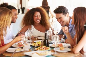 A group of friends smile and laugh while enjoying a meal at a restaurant