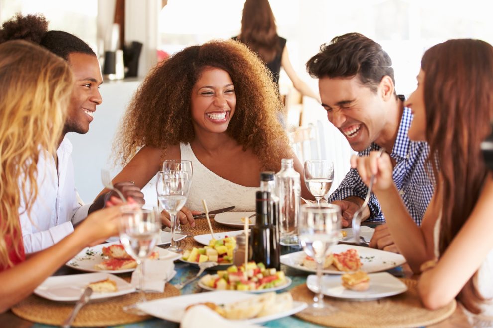 A group of friends smile and laugh while enjoying a meal at a restaurant