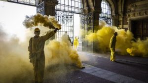 People in yellow boilersuits let off yellow smoke bombs.