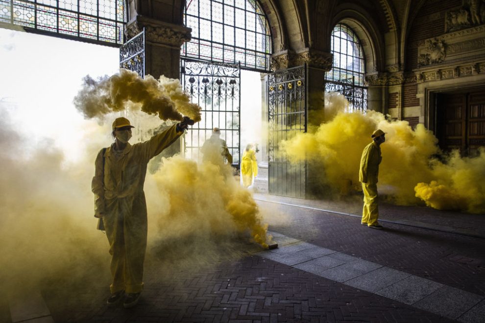 People in yellow boilersuits let off yellow smoke bombs.