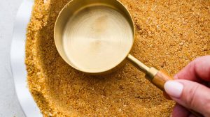 Overhead shot of someone pressing a measuring cup into the homemade graham cracker crust.