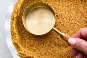 Overhead shot of someone pressing a measuring cup into the homemade graham cracker crust.