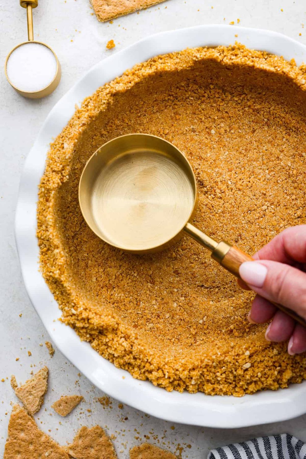 Overhead shot of someone pressing a measuring cup into the homemade graham cracker crust.