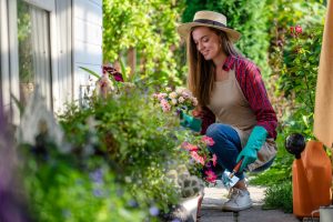 happy gardening woman in gloves, hat and apron plants flowers on the flower bed in home garden.