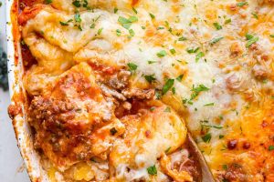 Overhead shot of million dollar ravioli casserole with wooden spoon scooping out a portion.