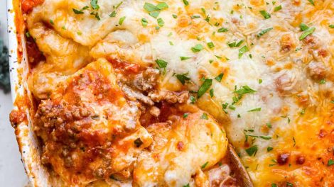 Overhead shot of million dollar ravioli casserole with wooden spoon scooping out a portion.