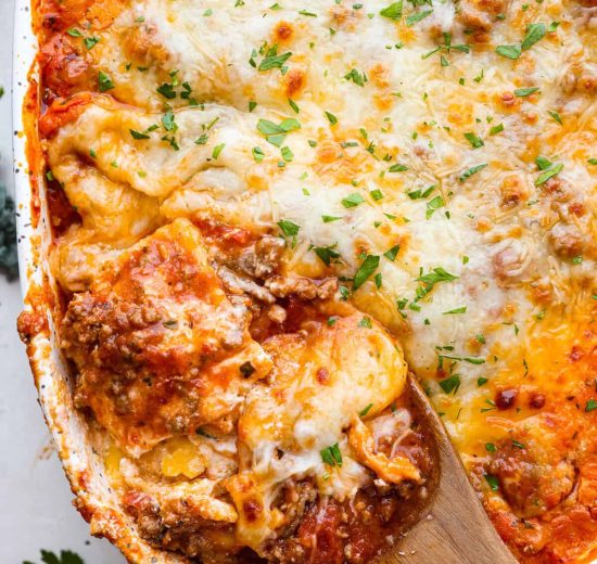 Overhead shot of million dollar ravioli casserole with wooden spoon scooping out a portion.