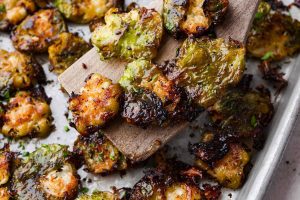 Angle shot of a wooden spatula holding up a few smashed Brussels sprouts out of the pan.