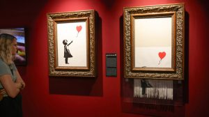 A woman looks at two paintings in a gallery with red walls.