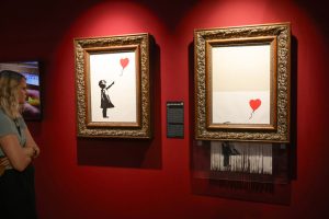 A woman looks at two paintings in a gallery with red walls.