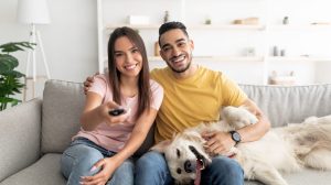 Couple sitting on couch with their dog, watching TV at home