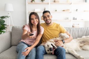 Couple sitting on couch with their dog, watching TV at home