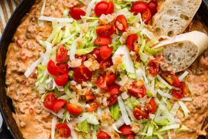 Overhead shot of cheeseburger dip topped with lettuce and tomatoes.