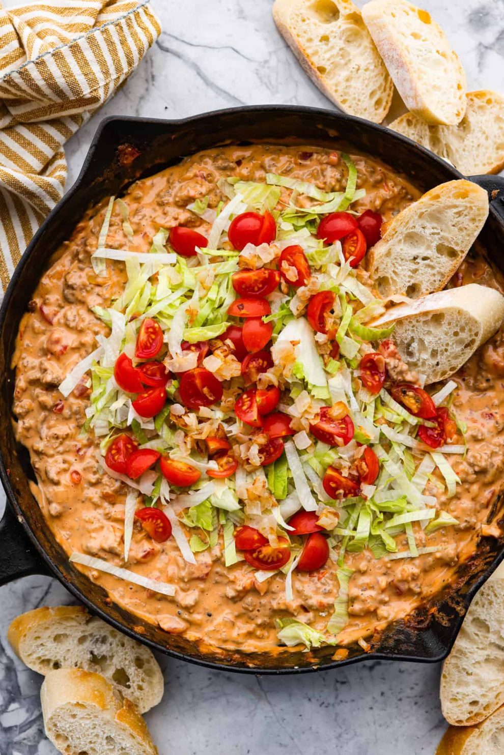 Overhead shot of cheeseburger dip topped with lettuce and tomatoes.