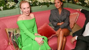 Two smiling women sit on a pink sofa.