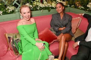 Two smiling women sit on a pink sofa.