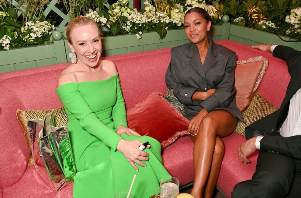 Two smiling women sit on a pink sofa.