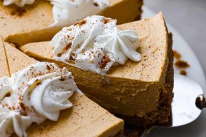 Angle shot of someone taking a slice of the no-bake pumpkin cheesecake with whipped cream on top.