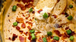 Close up shot of someone dipping a sliced baguette piece into the slow cooker crack chicken dip.