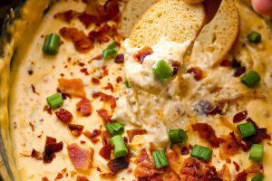 Close up shot of someone dipping a sliced baguette piece into the slow cooker crack chicken dip.